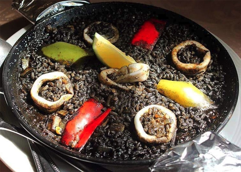 paella negra from ilustrado topped with bell peppers, squid, and lime