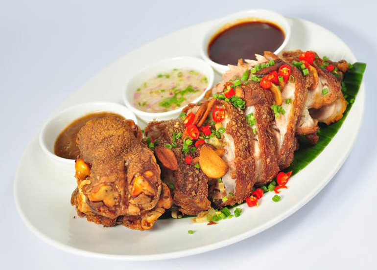Boneless Crispy Pata topped with chili, chives, and garlic with sides of vinegar and liver sauce from Tipulo Filipino